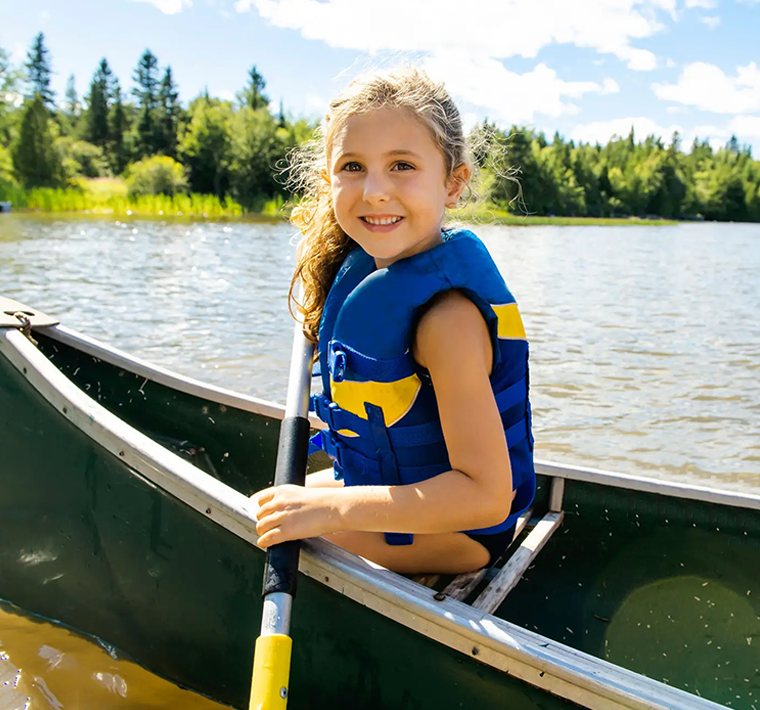 A young girl wearing a life jacket is sitting in a canoe on a lake