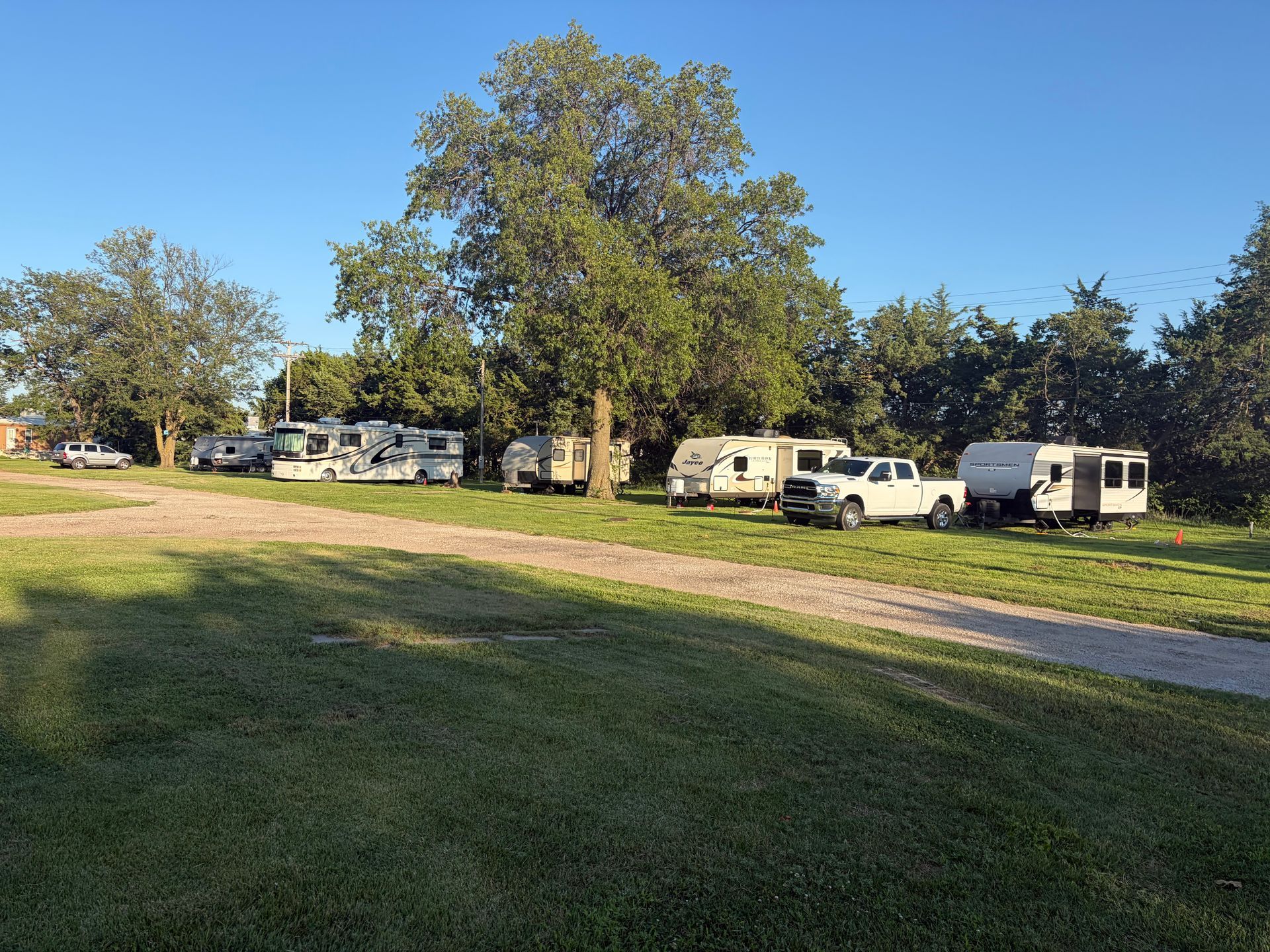 RVs and vans parked along a grassy field beside a dirt road under a clear blue sky