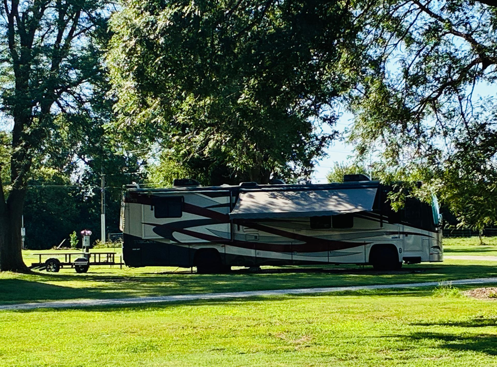 Large white RV parked on a grassy field under trees on a sunny day