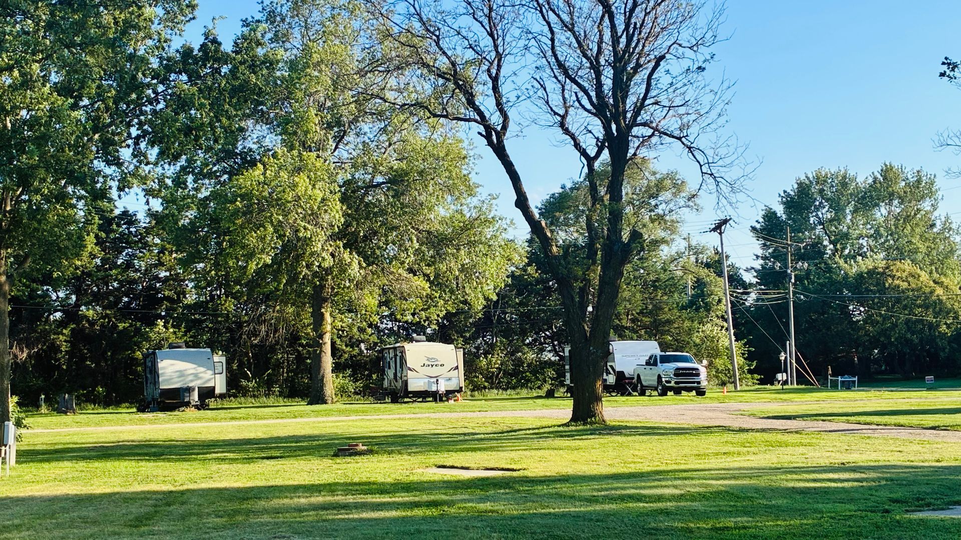 Three RVs parked on a grassy field with trees under a clear blue sky.