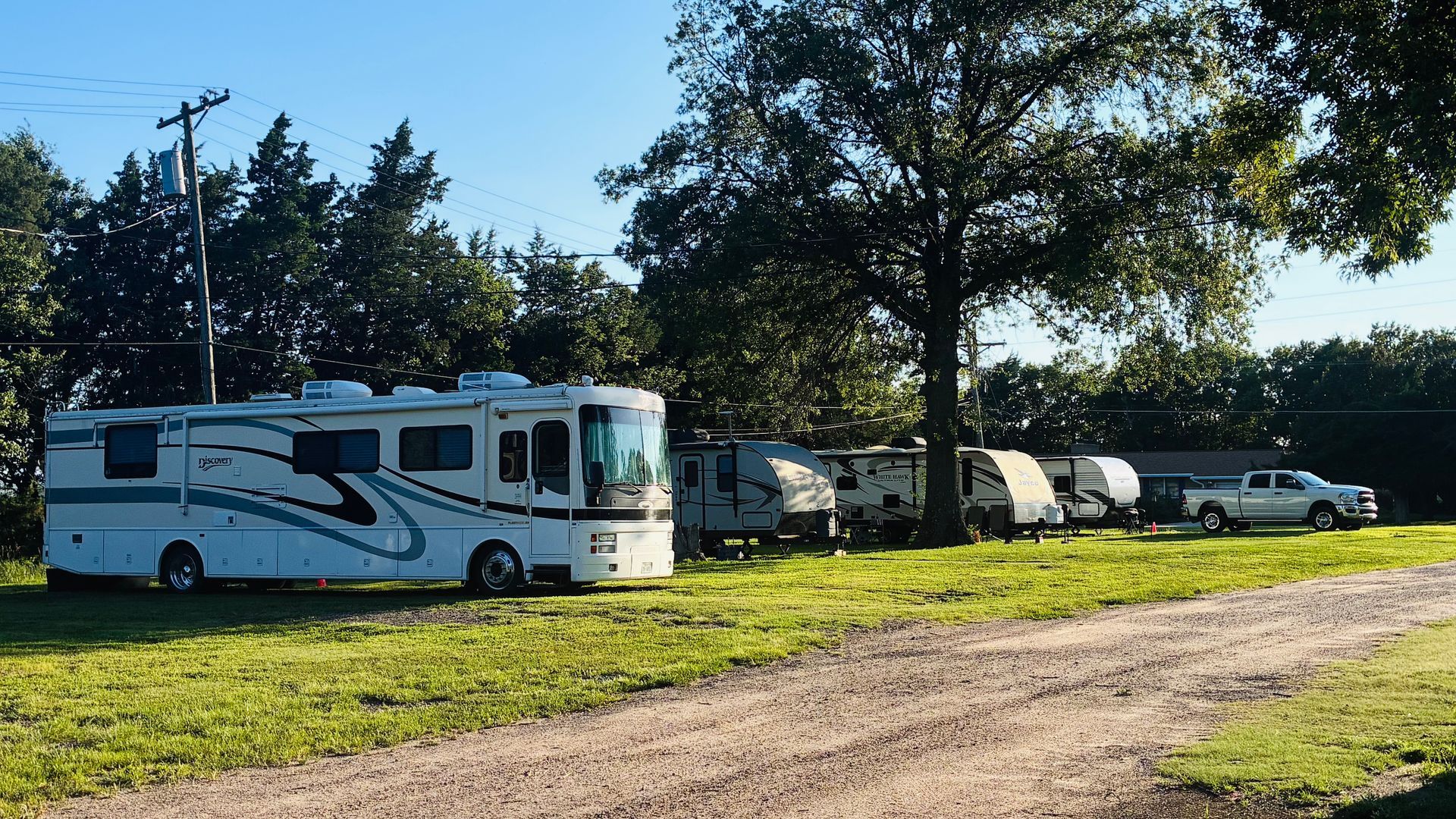 RV parked on a grassy campsite with trees and other trailers in the background