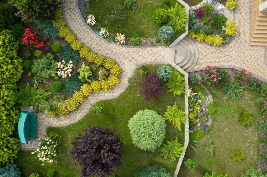 Top-down view of a landscaped garden with winding stone paths, colorful flowers, shrubs, and a bench