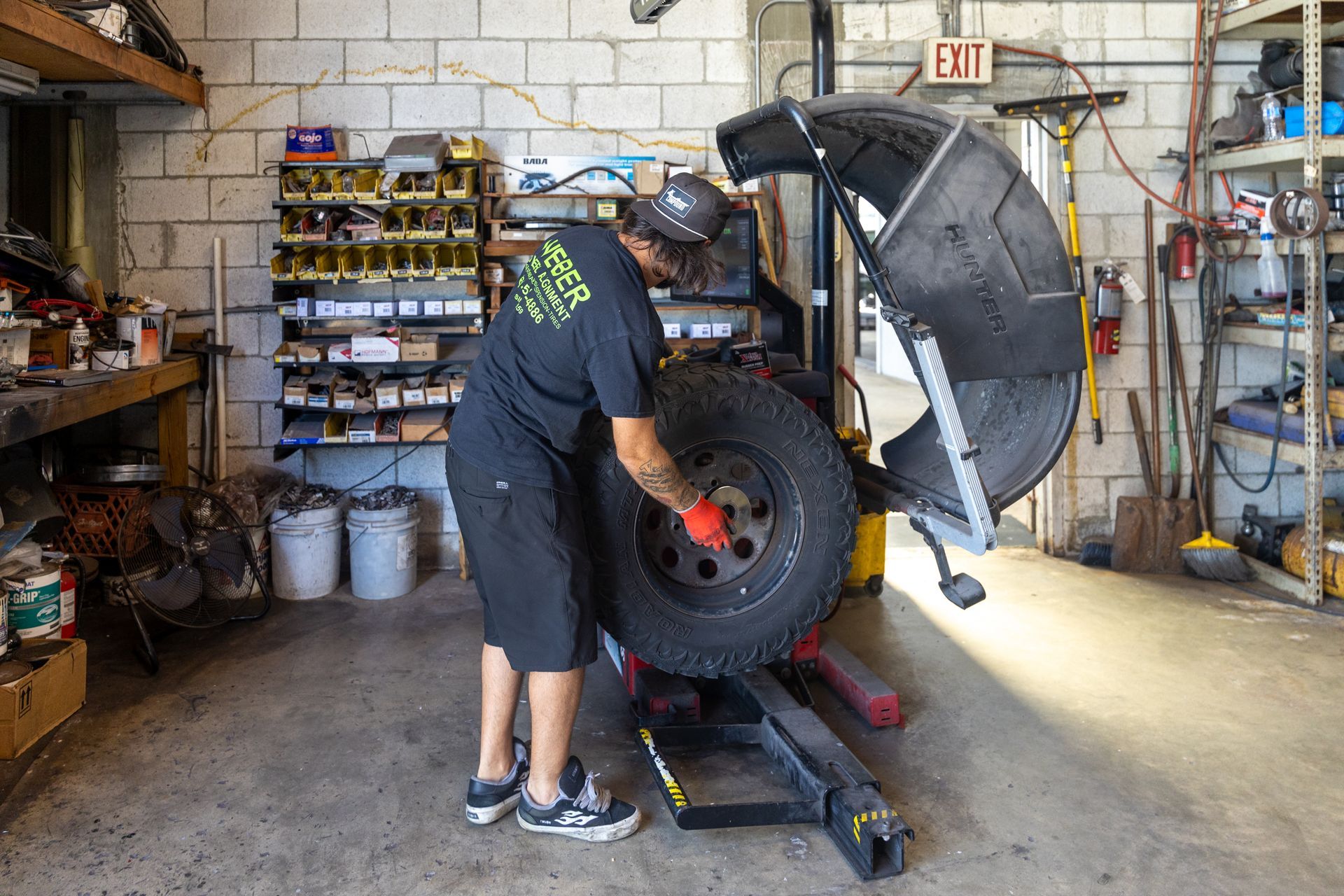 Mechanic repairing a vehicle in a garage, working on a lifted tire and open hood.
