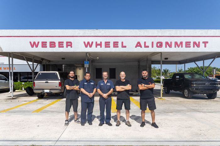 Five workers standing outside Weber Wheel Alignment garage under red signage