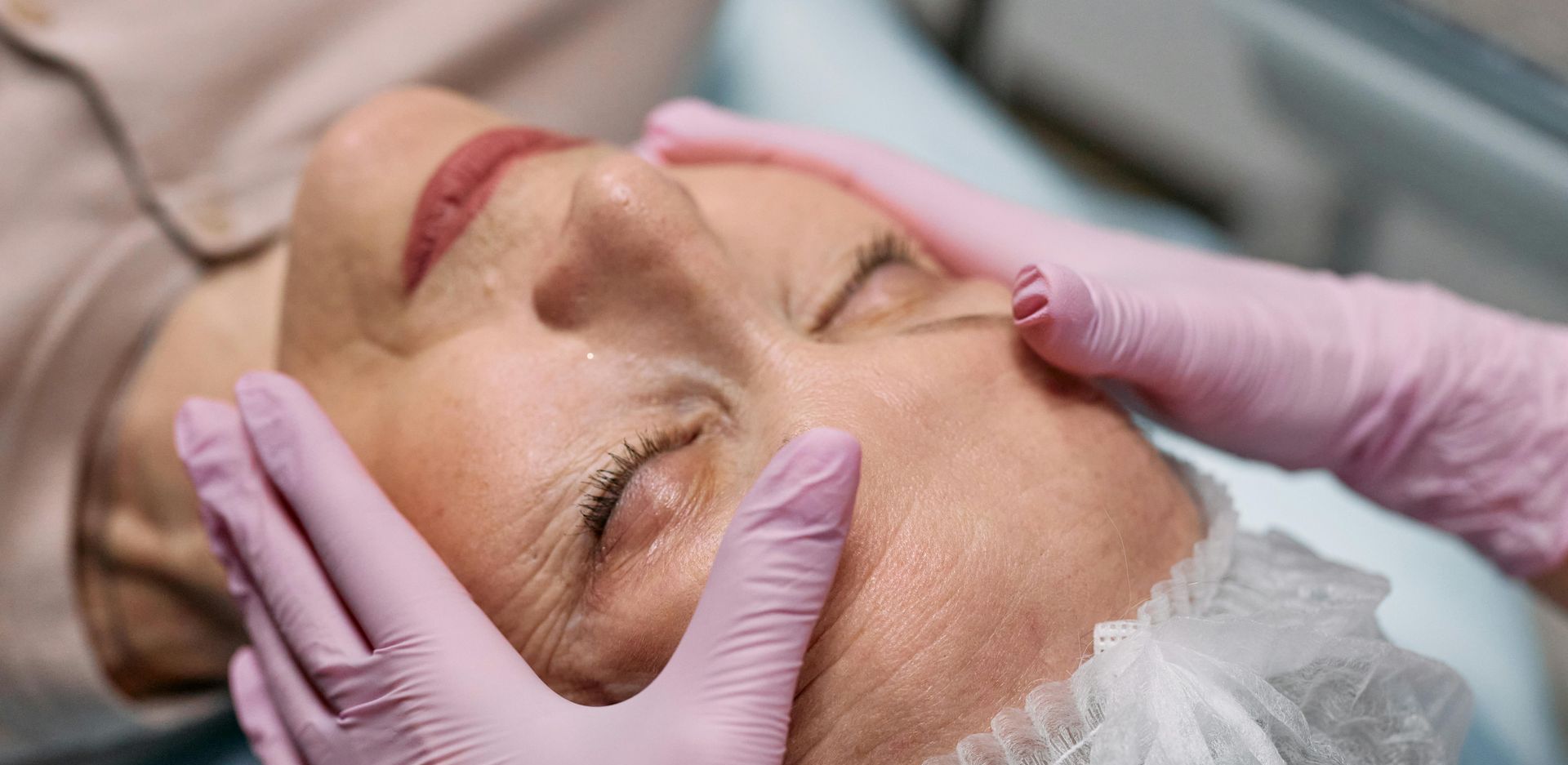technician with light pink gloves massages woman's face in spa setting