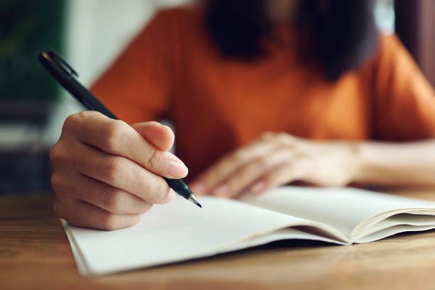 A woman is writing in a notebook with a pen.