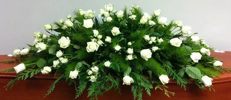 A large arrangement of white roses and greenery on a wooden table.