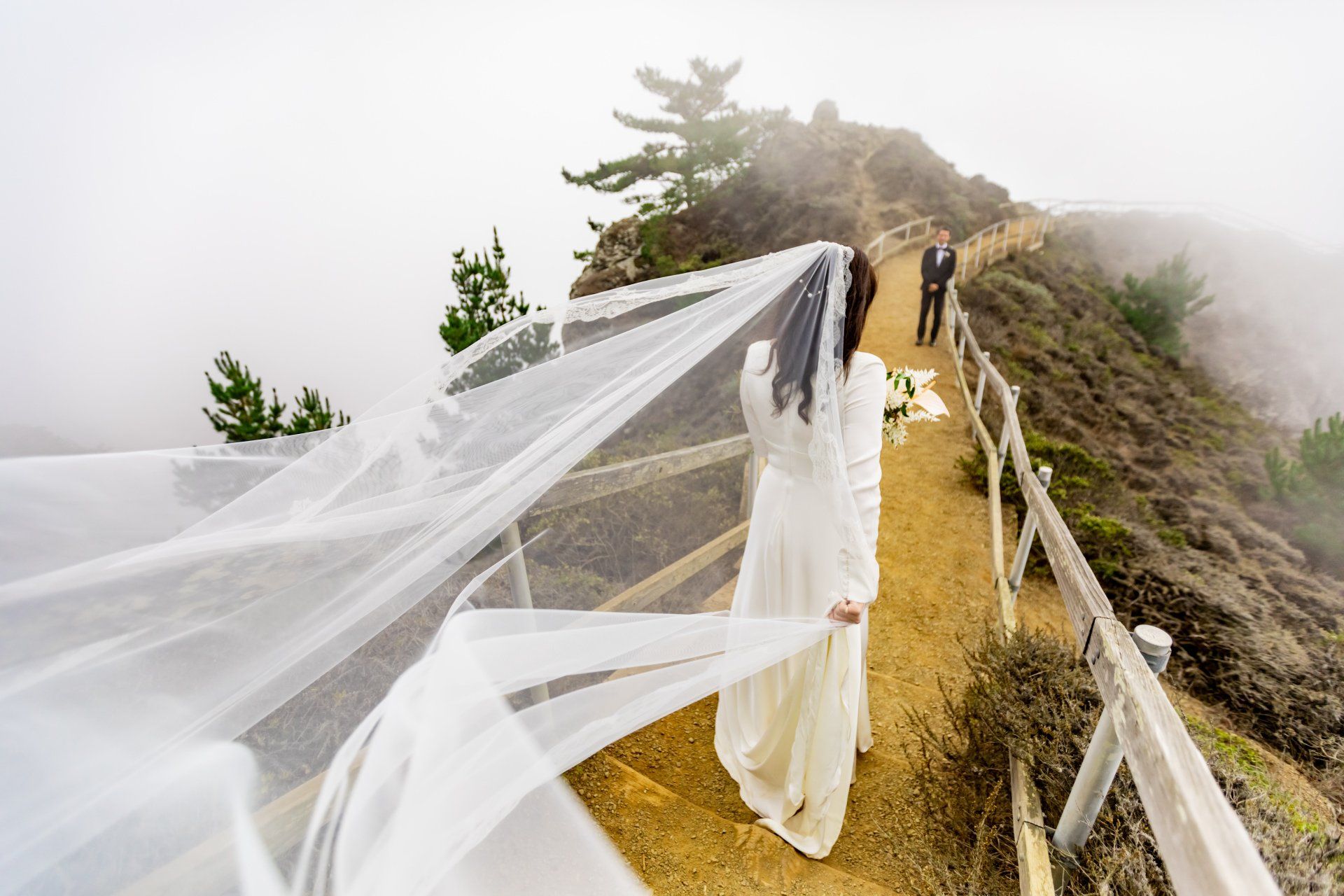 A bride in a wedding dress and veil is walking down a path.