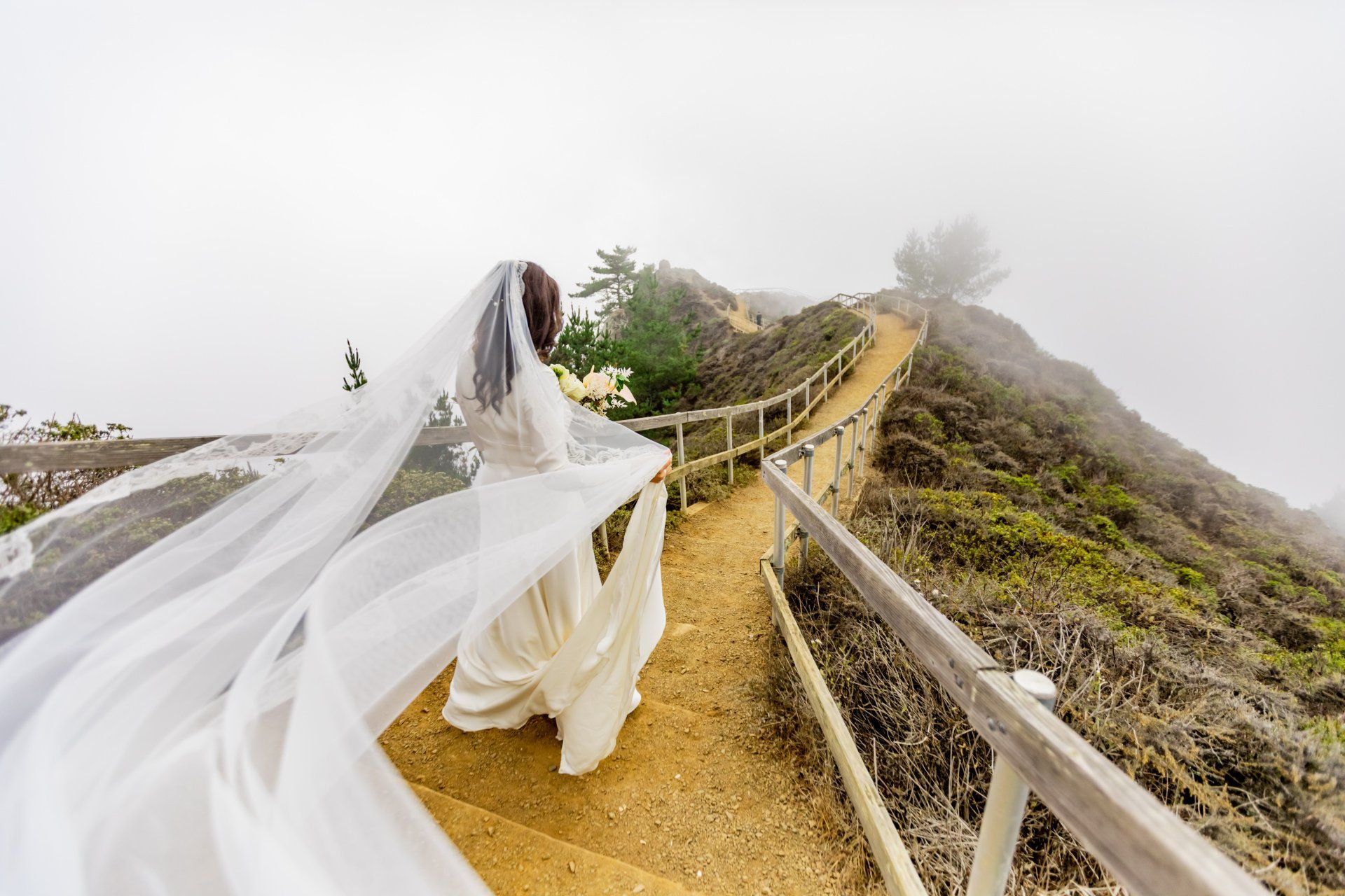 A bride in a wedding dress and veil is walking down a path.