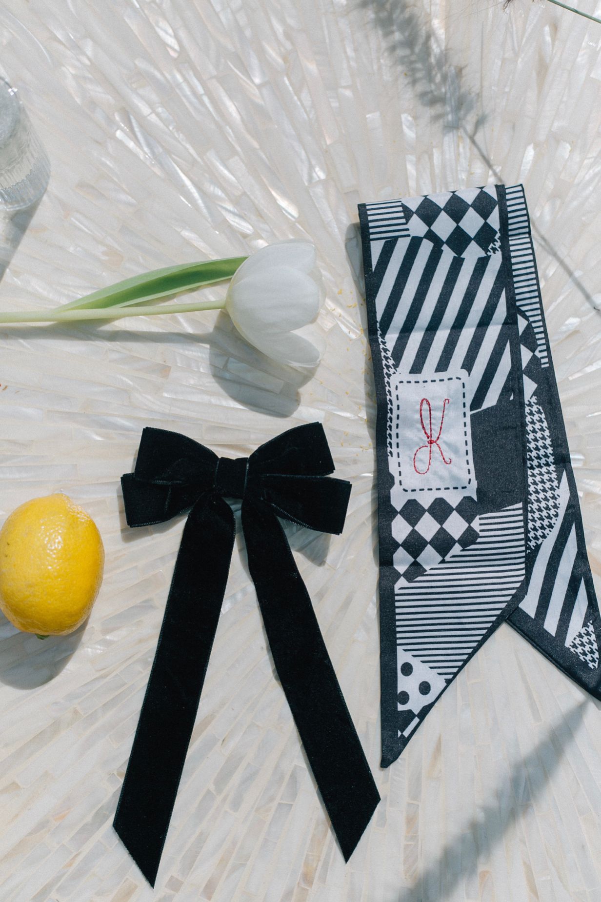 Black ribbon bow, striped necktie, white tulip, and lemon on a light surface