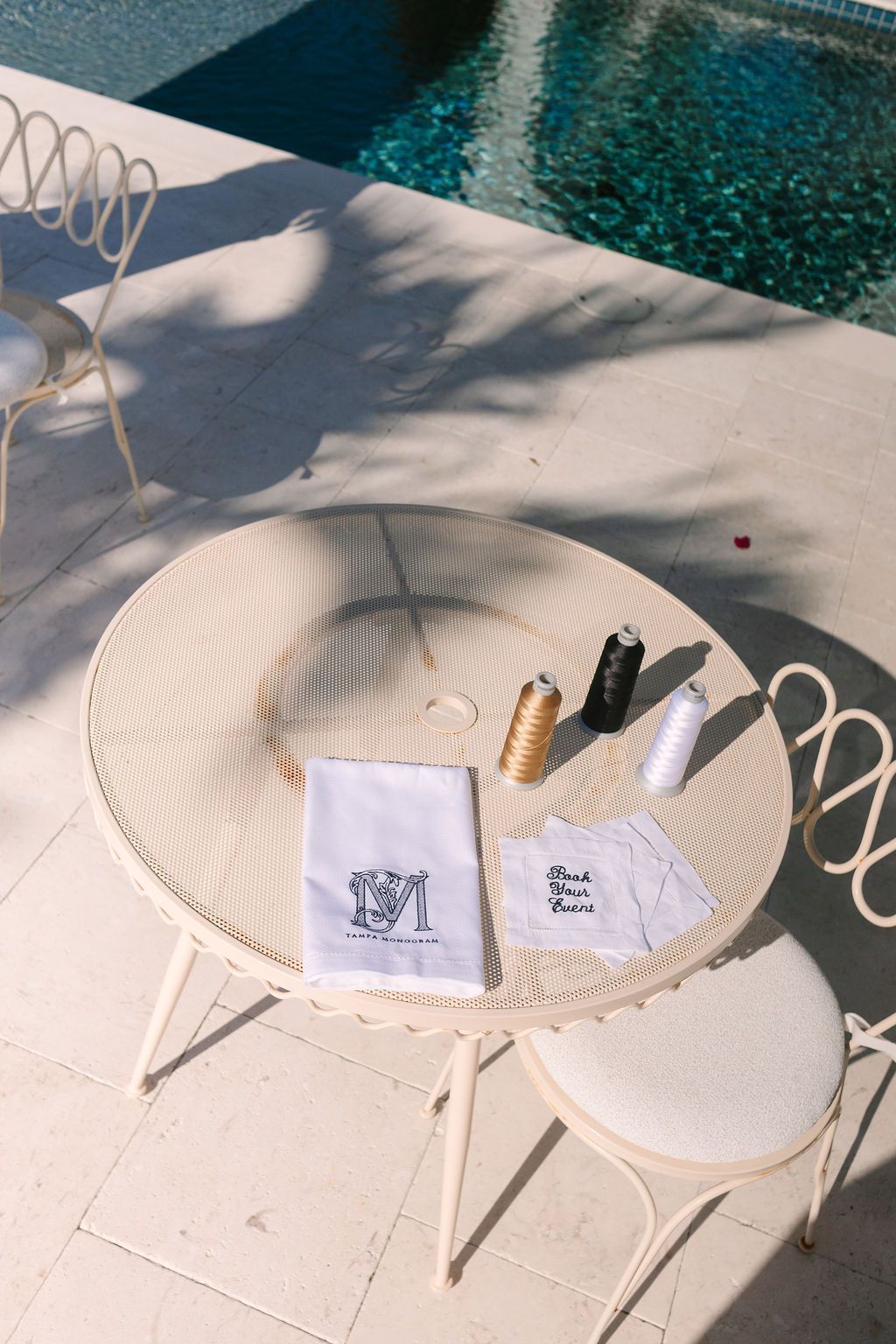 White patio table and chairs by a pool, with papers and bottles on the table.