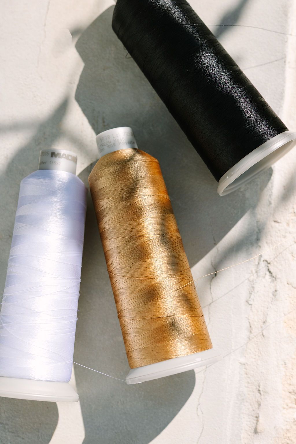 Three spools of thread in white, gold, and black on a light marble surface