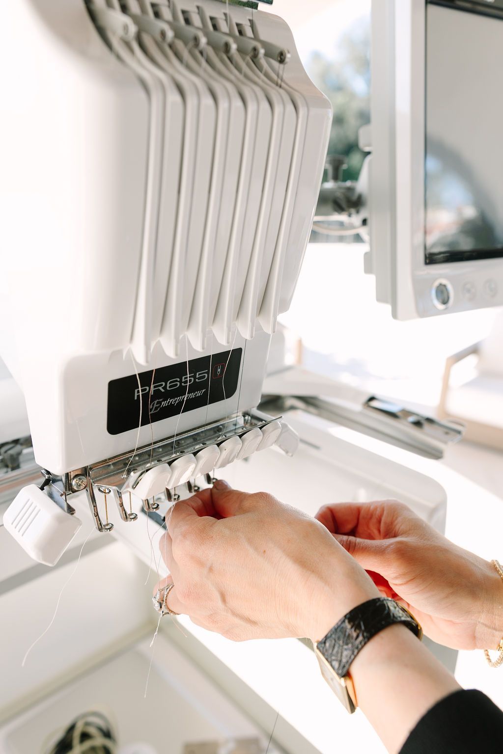 Hands adjusting white industrial sewing machine controls in a bright workspace