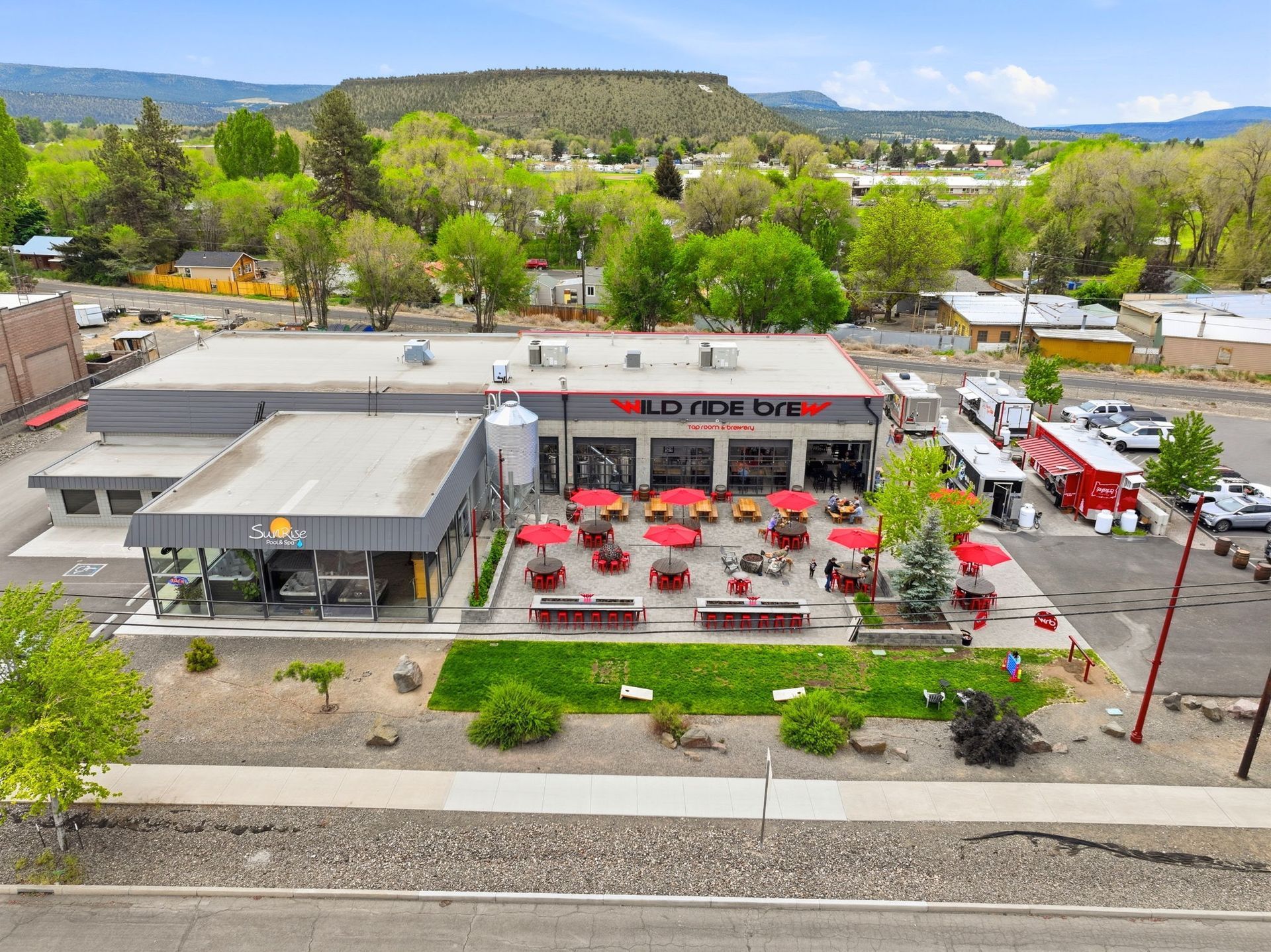 Aerial view of a roadside restaurant with red patio umbrellas, surrounded by trees and hills.