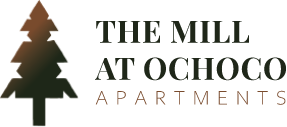 The Mill at Ochoco Apartments logo in dark charcoal featuring a bold pine tree icon and serif property name.