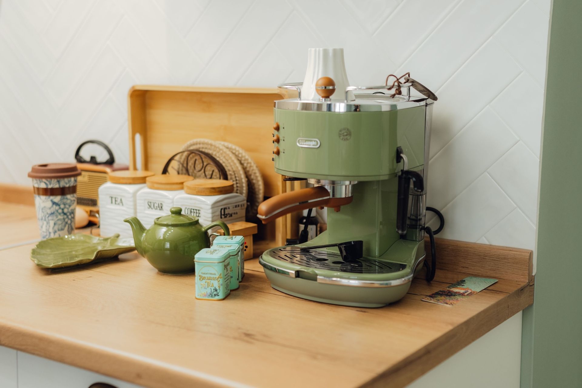 A green coffee maker sits on a kitchen counter, surrounded by coffee mugs and accessories.