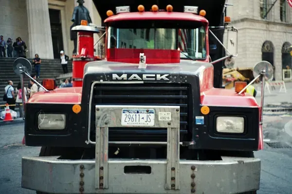 Red Mack truck facing camera at a city street event, with chrome grill and red cab.