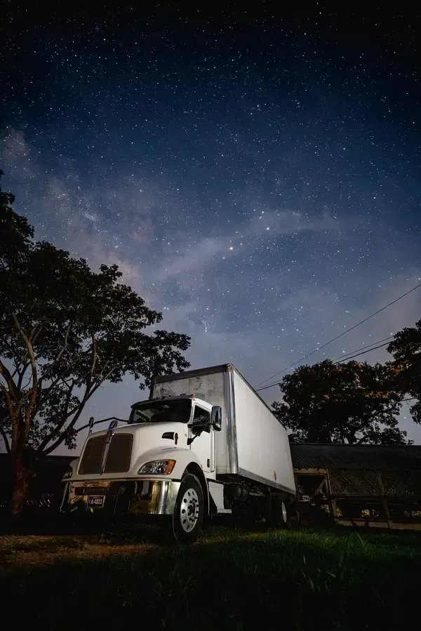 White box truck parked under a starry night sky with silhouetted trees