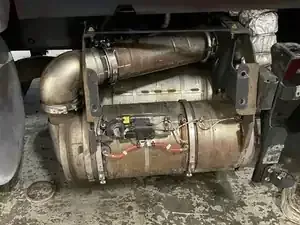Metal exhaust and cylindrical tank assembly mounted under a vehicle chassis, with pipes and wiring visible