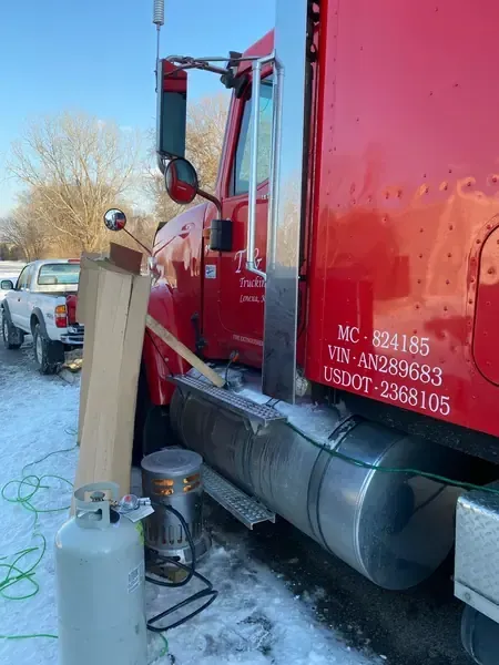 Red semi-truck parked in snow beside a wooden post and a small propane tank