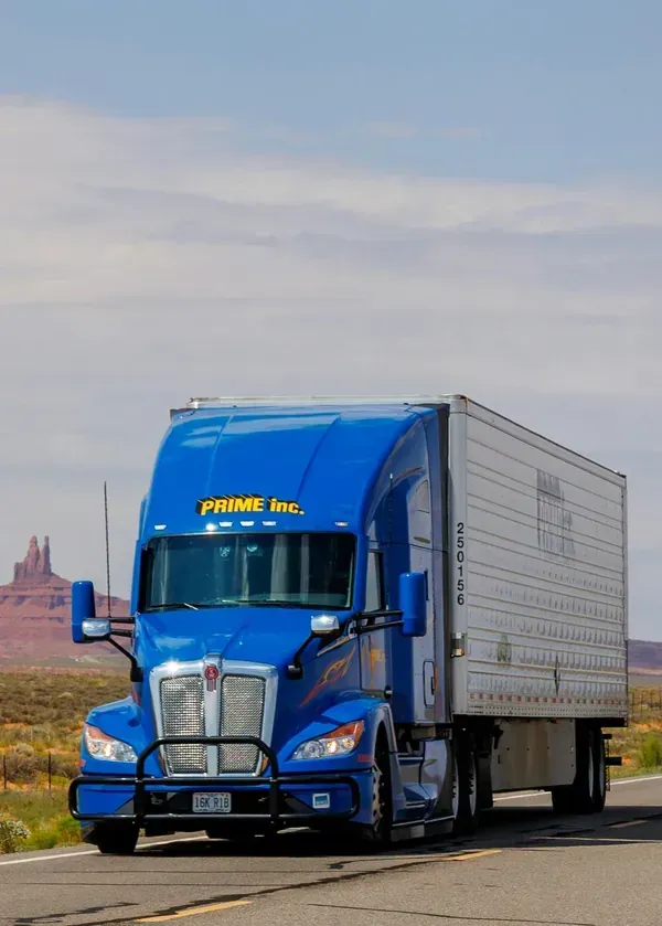 Blue semi truck with a white trailer driving on a desert highway under a cloudy sky