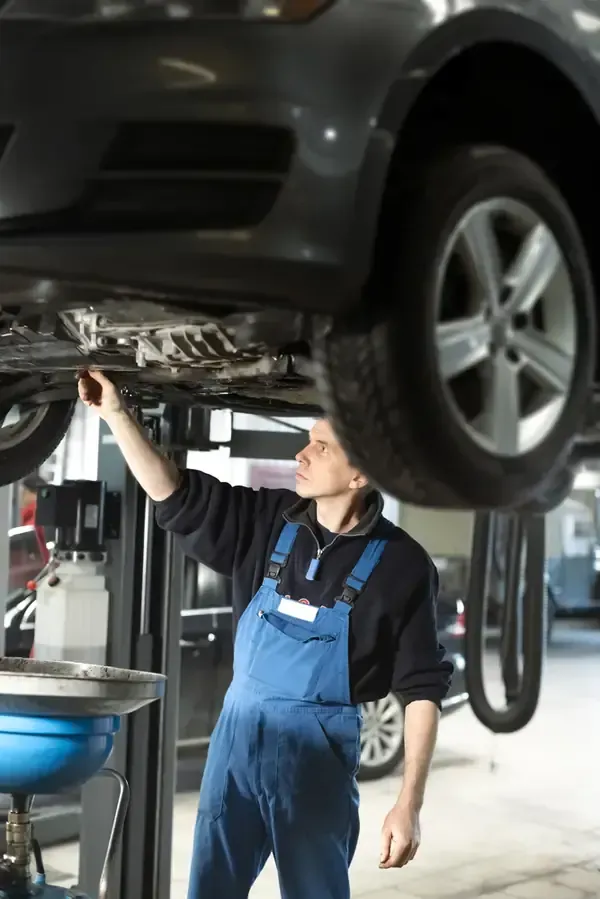 Mechanic in blue overalls inspecting the underside of a car on a lift in a garage