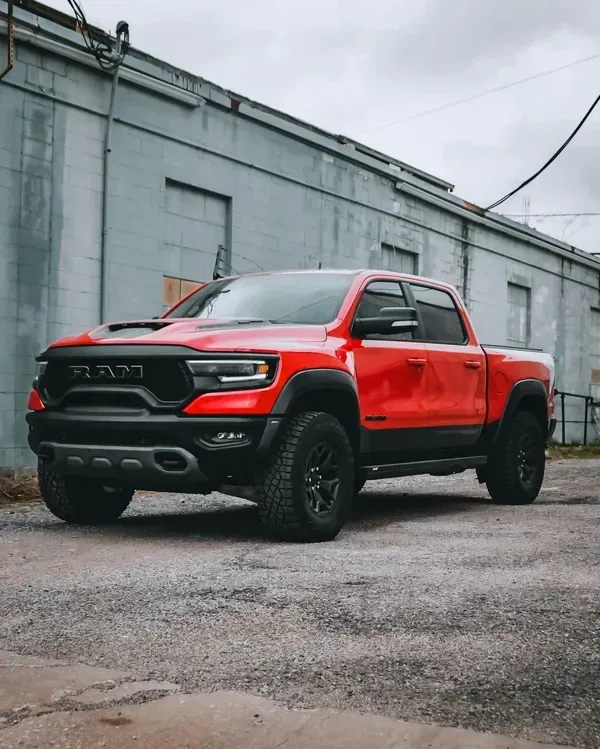 Red Ram pickup truck parked on wet pavement beside an industrial building