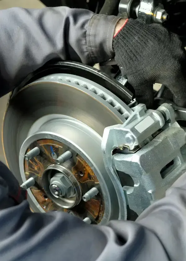 Gloved hands inspecting a car brake rotor and caliper assembly in a workshop