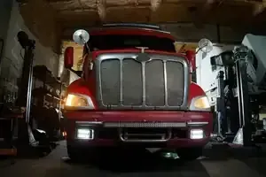 Red semi truck parked in a garage, facing forward with headlights on.