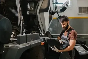 Mechanic using a tablet beside a large truck in a repair garage