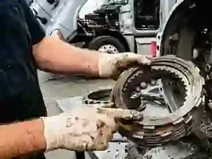 Mechanic holding a greasy metal clutch assembly in a workshop next to a vehicle lift