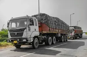 White cargo truck hauling a tarped load on a road with another truck behind it