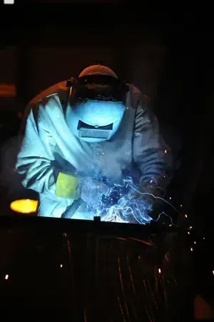 Welder in protective gear welding metal, bright sparks flying in a dark workshop