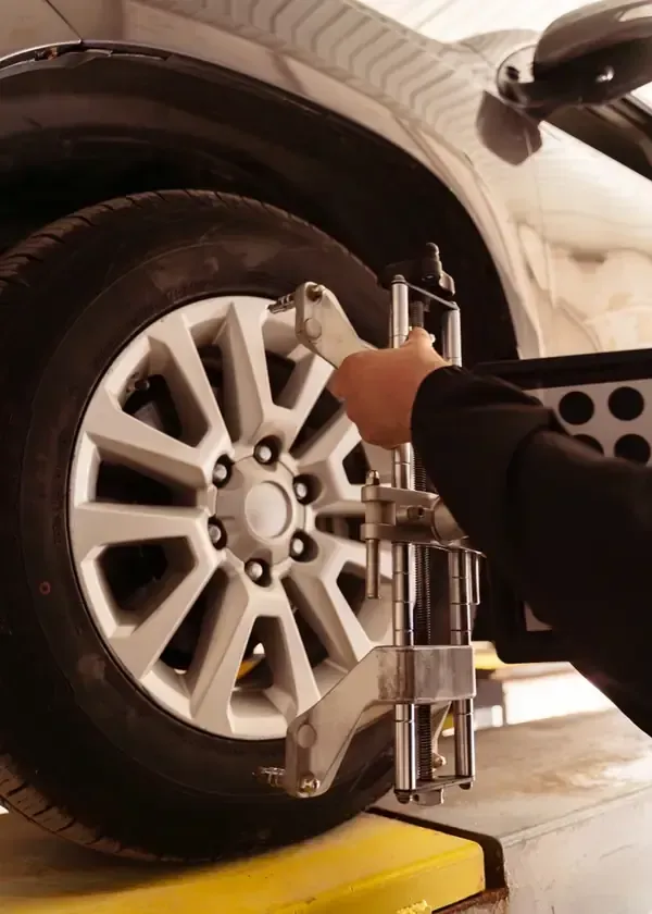 Mechanic using a jack to lift a white car’s front wheel in a garage