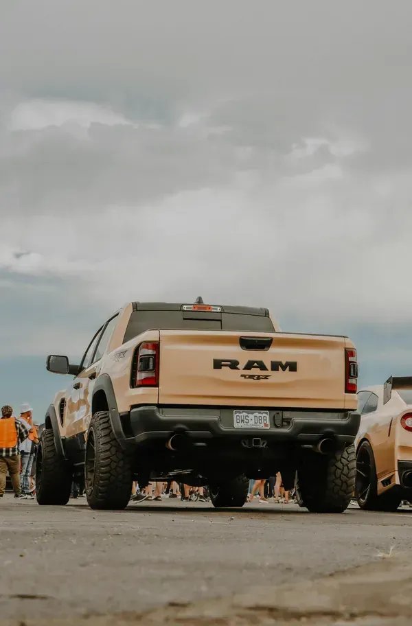 Beige RAM pickup truck parked outdoors at a car meet under a cloudy sky