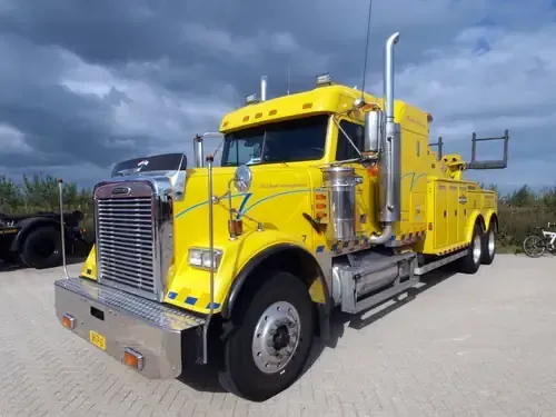 Yellow tow truck parked outdoors under cloudy sky