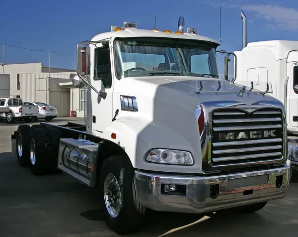 White Mack semi-truck parked outdoors in a lot, front and side view