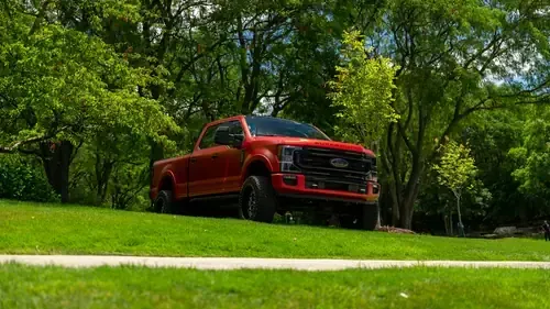Red pickup truck parked on a grassy lawn with trees in the background.