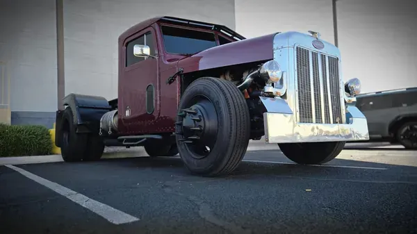 Maroon vintage pickup truck with chrome grille parked in a lot, low-angle view