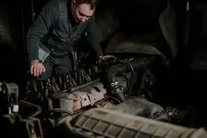 Man inspecting a car engine in a dim garage, leaning over the open hood.