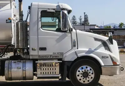 White semi-truck cab with silver tank parked outdoors on a sunny day