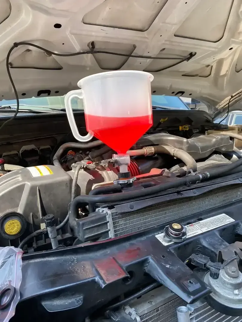 Red funnel filled with fluid pouring into a car engine bay under an open hood.