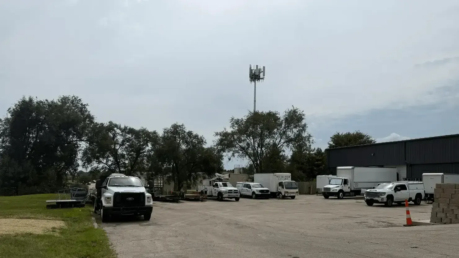 Parking lot with several white trucks and vans beside a dark warehouse under a cloudy sky