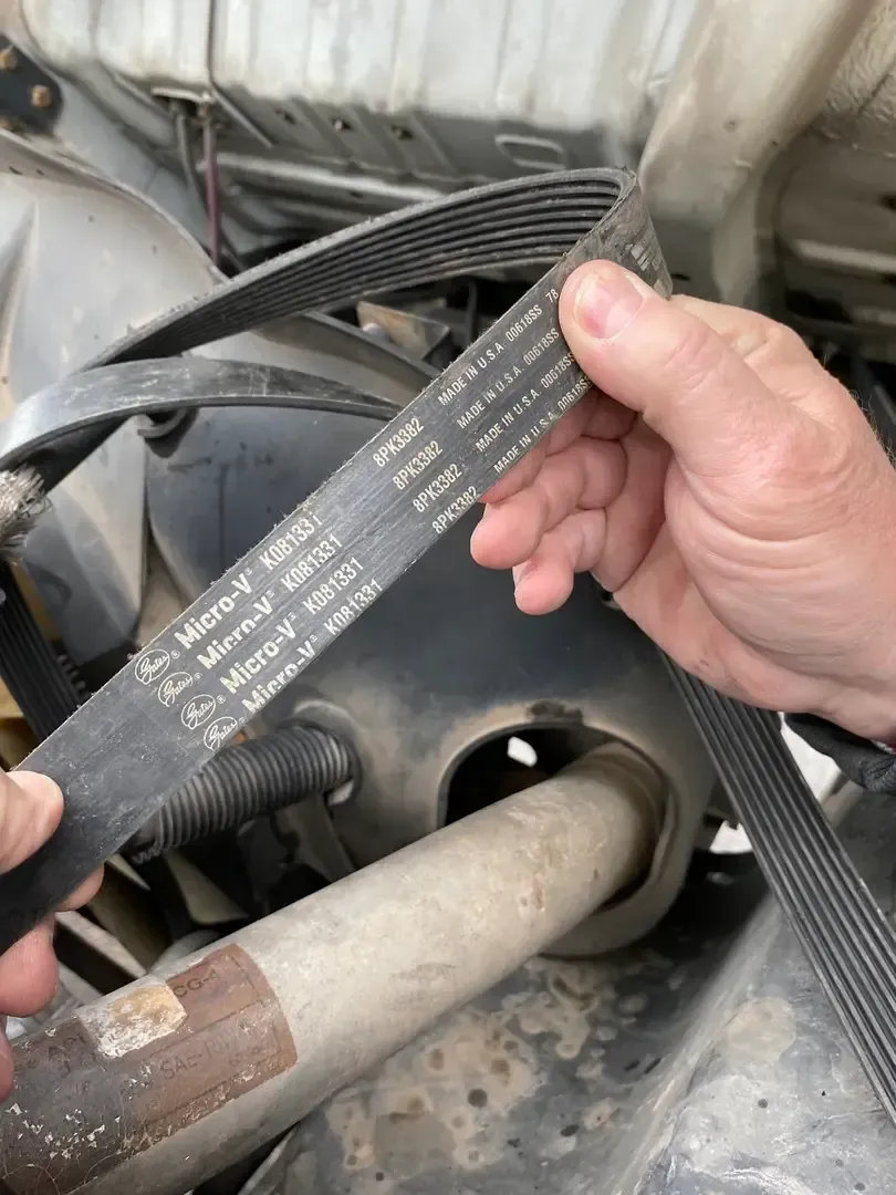 Hand holding a worn serpentine belt near a car engine compartment