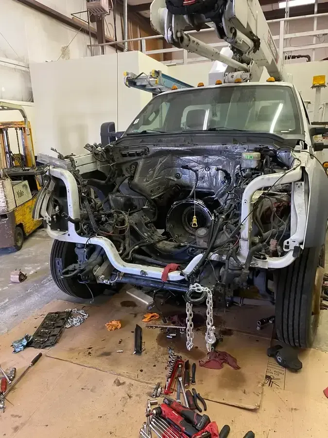 Partially disassembled car in an auto shop, front end removed and hanging tools visible