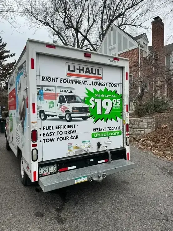 U-Haul truck parked on a residential street with trees and brick houses in the background.