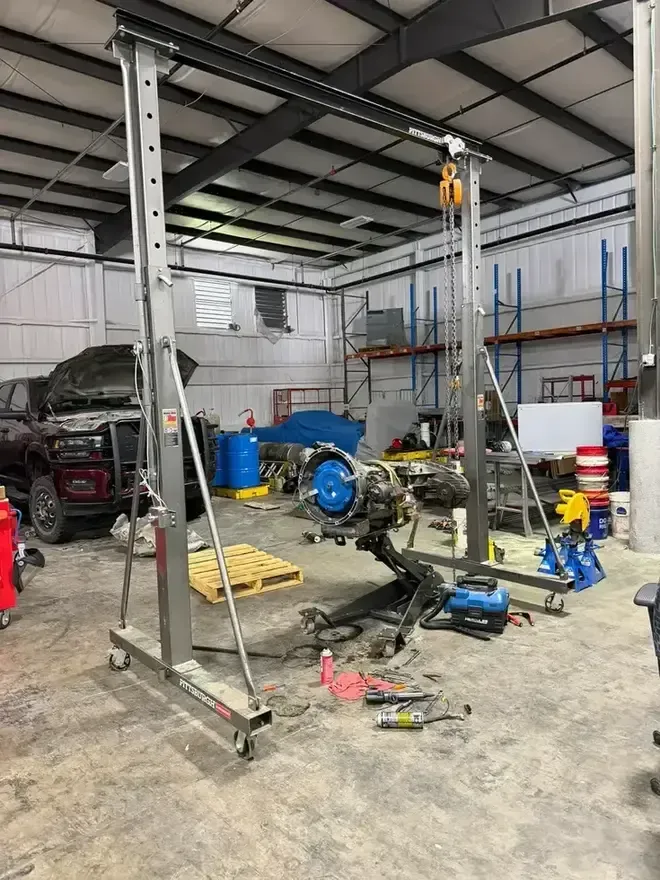 Mechanic working on a large engine in a garage, surrounded by car parts and tools
