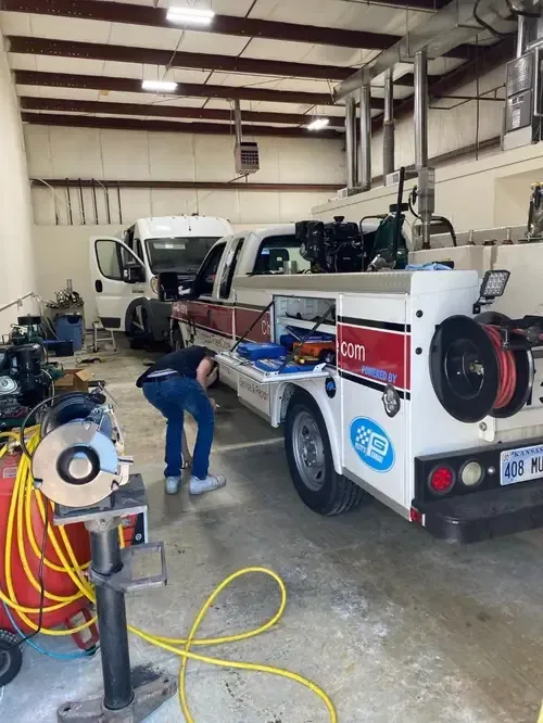 Tow truck bay with mechanic working beside a white tow truck in a garage.