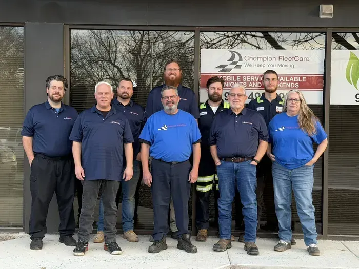 Six people in navy and blue shirts posing outside a Champion Fire & Security office.