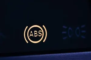 Dashboard close-up showing illuminated ABS warning light with dim blue icons рядом
